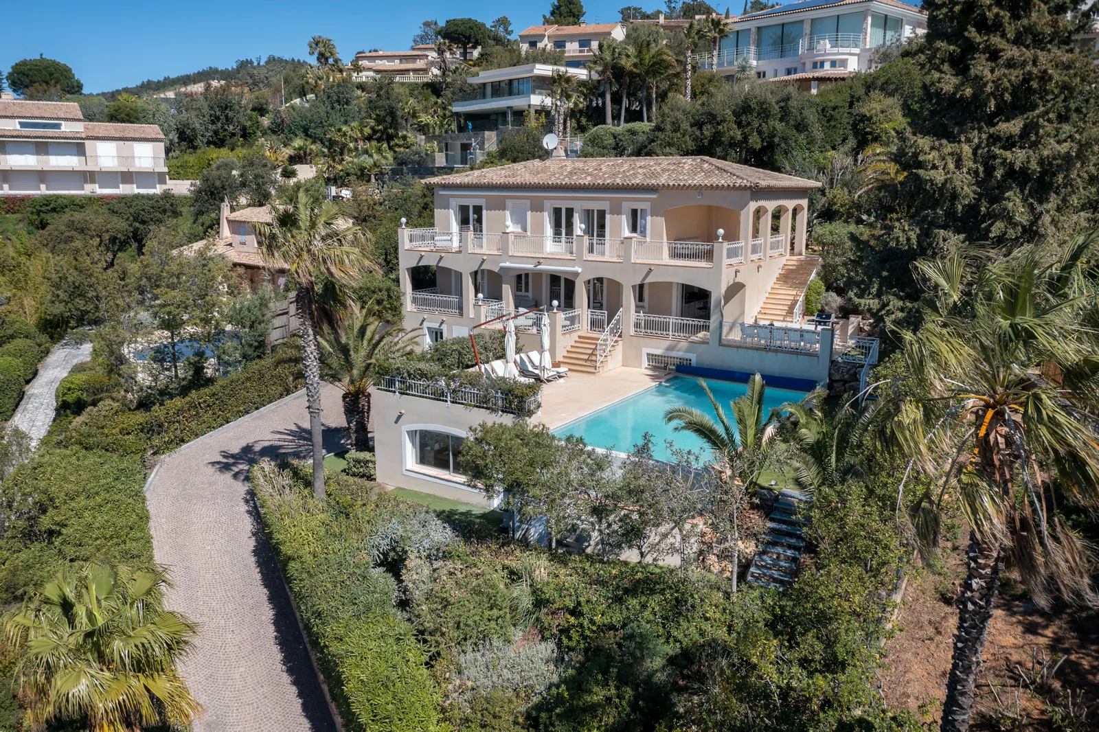 Vue aérienne de la villa à terrasses, piscine turquoise et palmiers.
